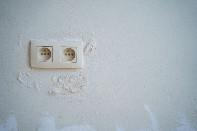 Mur avec prise électrique entouré de cloques dans la peinture dues à l'humidité.