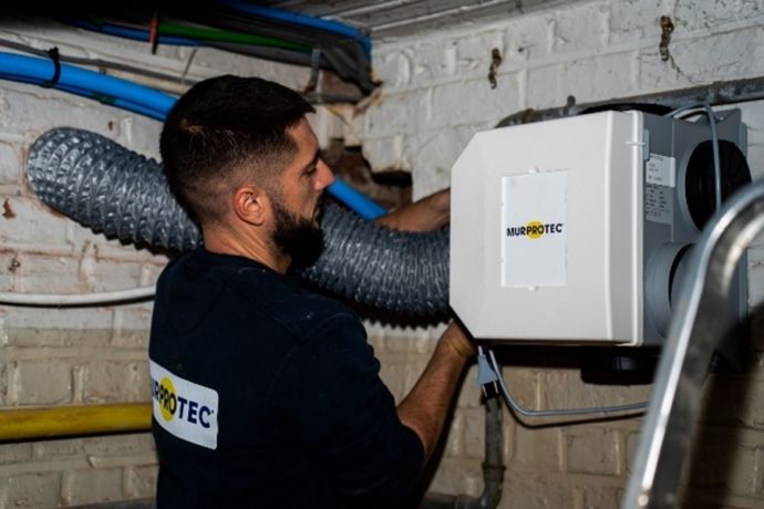Un installateur de Murprotec installe un système de traitement d'air dans la cave
