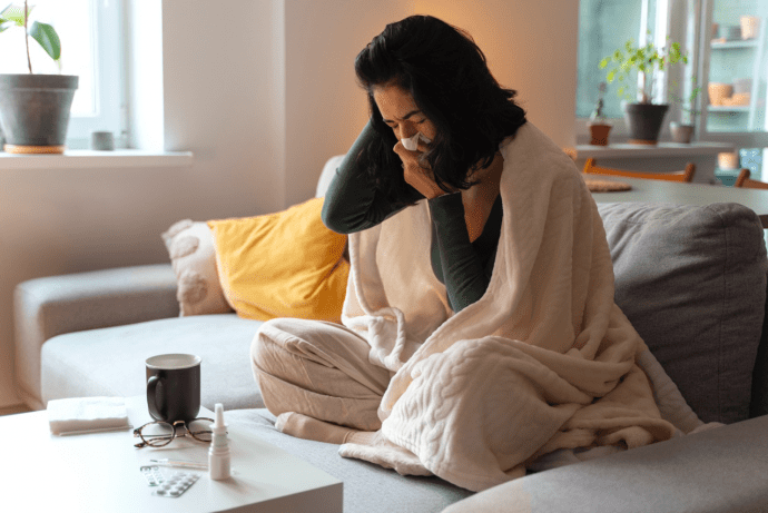 Une femme est assise sur le canapé avec une couverture et se mouche parce qu'elle est malade.