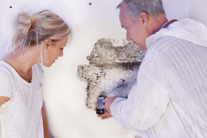 Un expert montre à une jeune femme l’humidité dans la maison par une analyse d’un mur