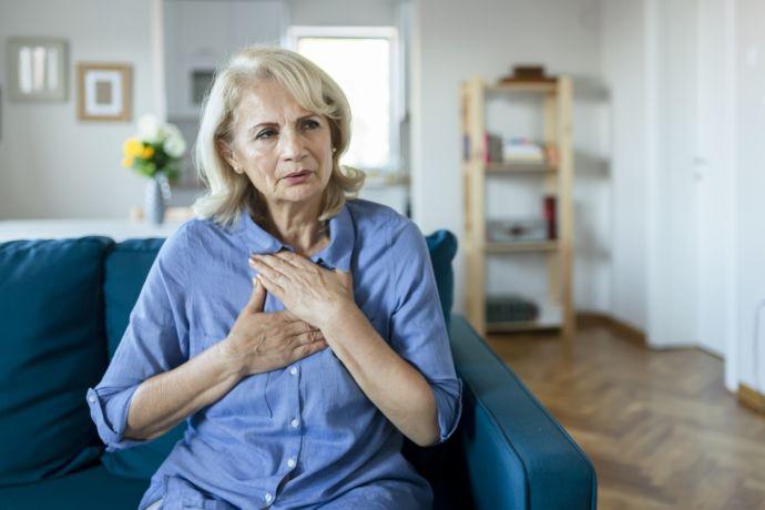 Oudere vrouw zit thuis op de sofa en heeft pijn op de borst