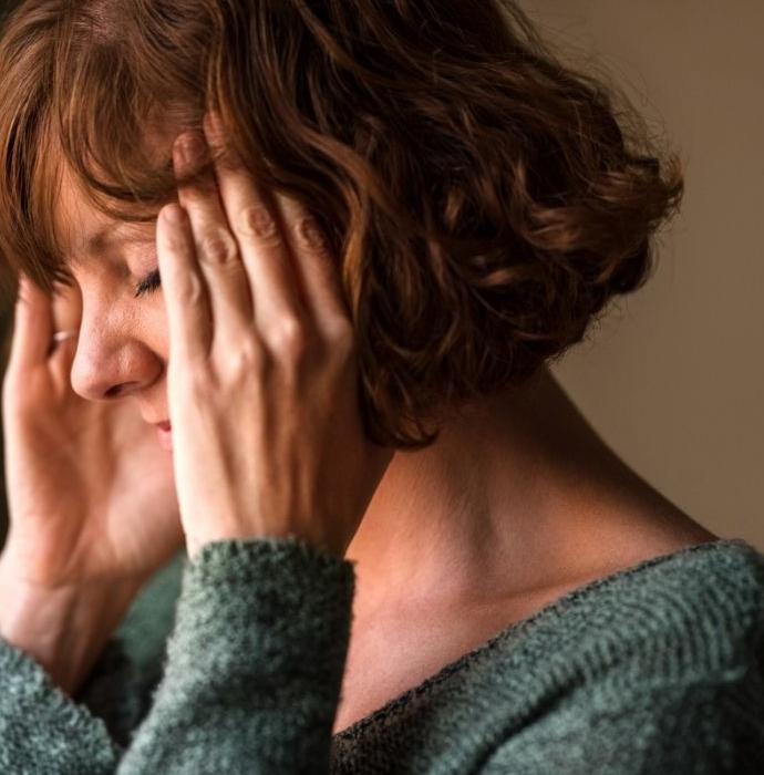 Vrouw met kort bruin haar heeft hoofdpijn en wrijft over haar slapen 