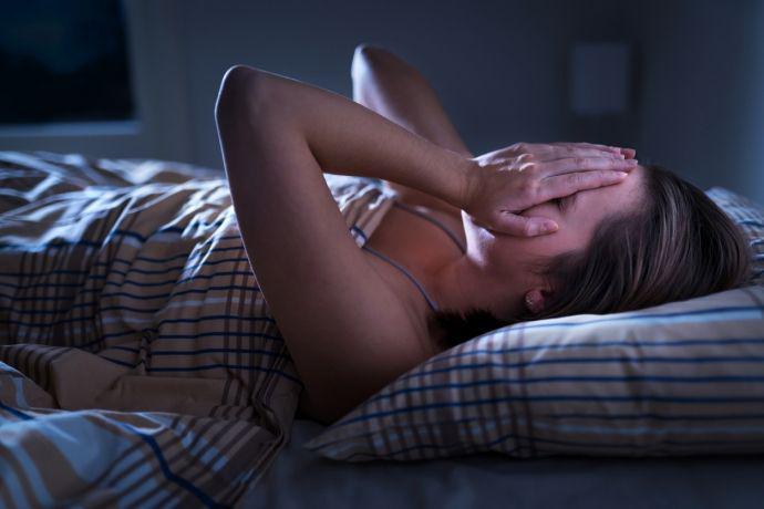 Une femme est réveillée la nuit par des maux de tête et se tient le visage dans les mains