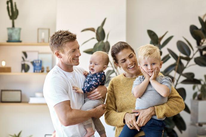 Couple de jeunes parents souriants dans leur salon avec chacun un enfant dans les bras