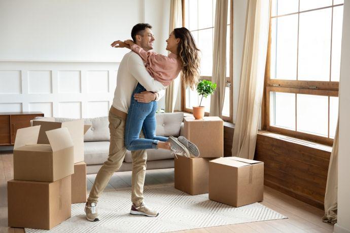 Un jeune couple qui vient d’emménager est enlacé dans son salon rempli de boîtes en carton