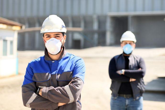 2 experts de Murprotec portant un casque et un masque antipoussière l'un en face de l'autre les bras croisés